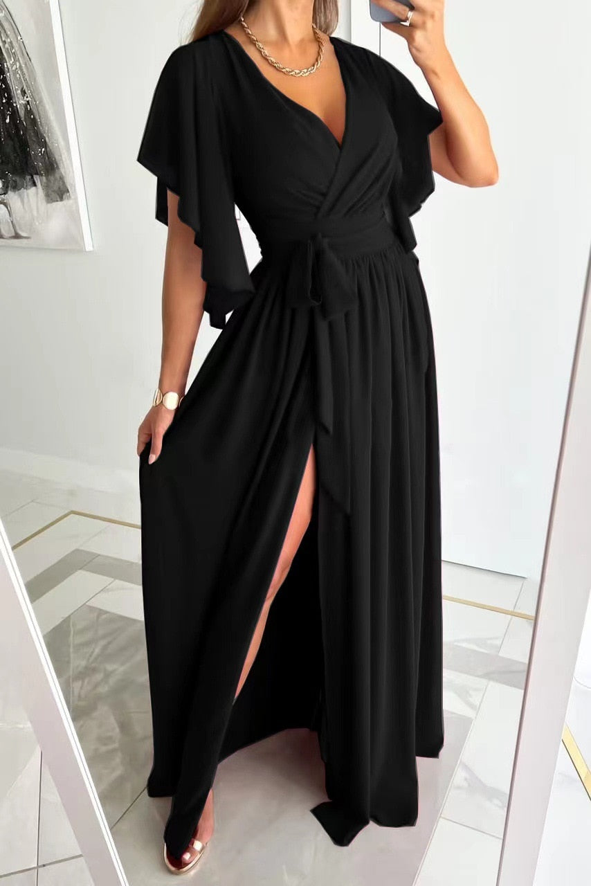 Modell steht in einem schwarzen Maxikleid mit Schlitz vorne.